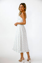 Side view of a woman wearing a white dress with blue floral patterns on a white background