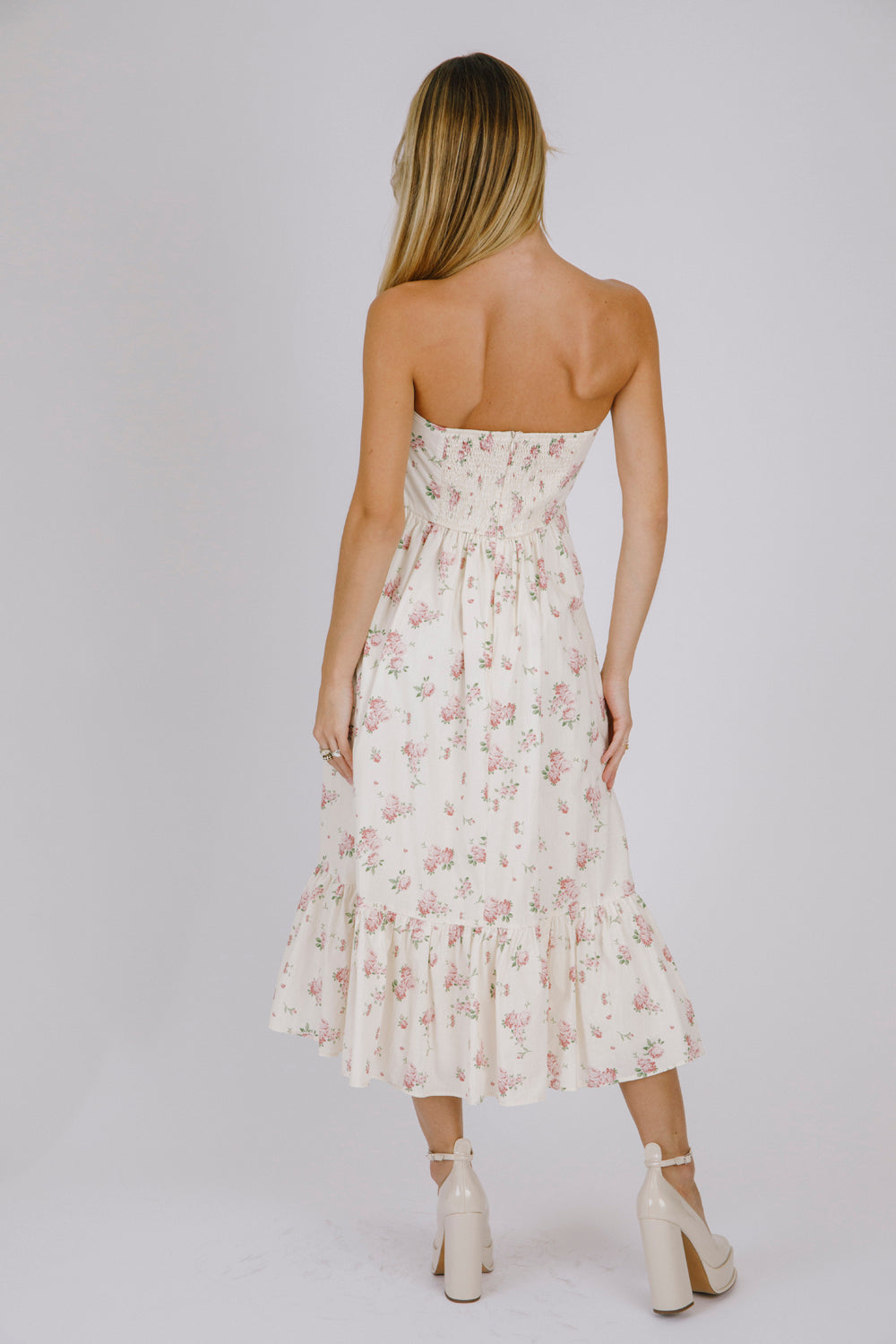 Back view of a woman wearing a strapless cream floral dress against a plain background