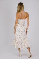 Back view of a woman wearing a strapless cream floral dress against a plain background
