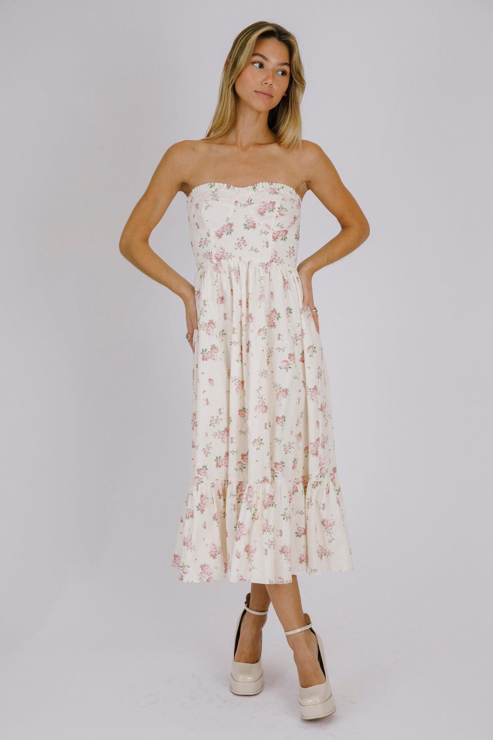 Woman wearing a strapless cream floral dress against a plain background