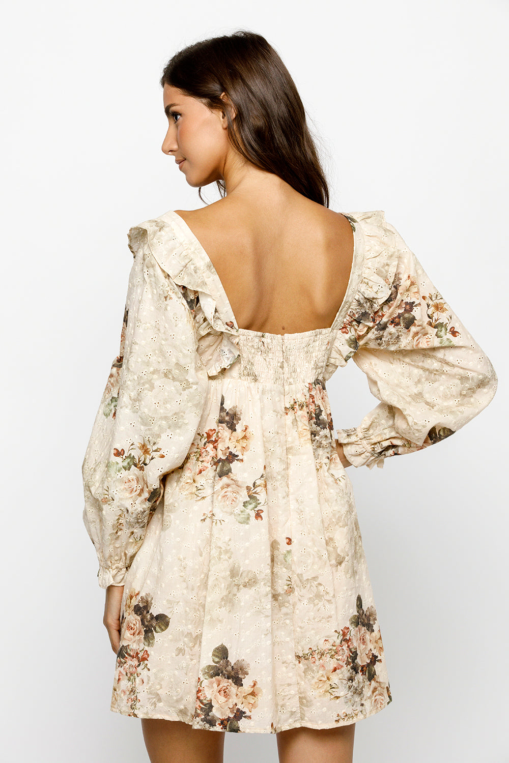 Back view of a woman wearing a beige floral dress with a plain background