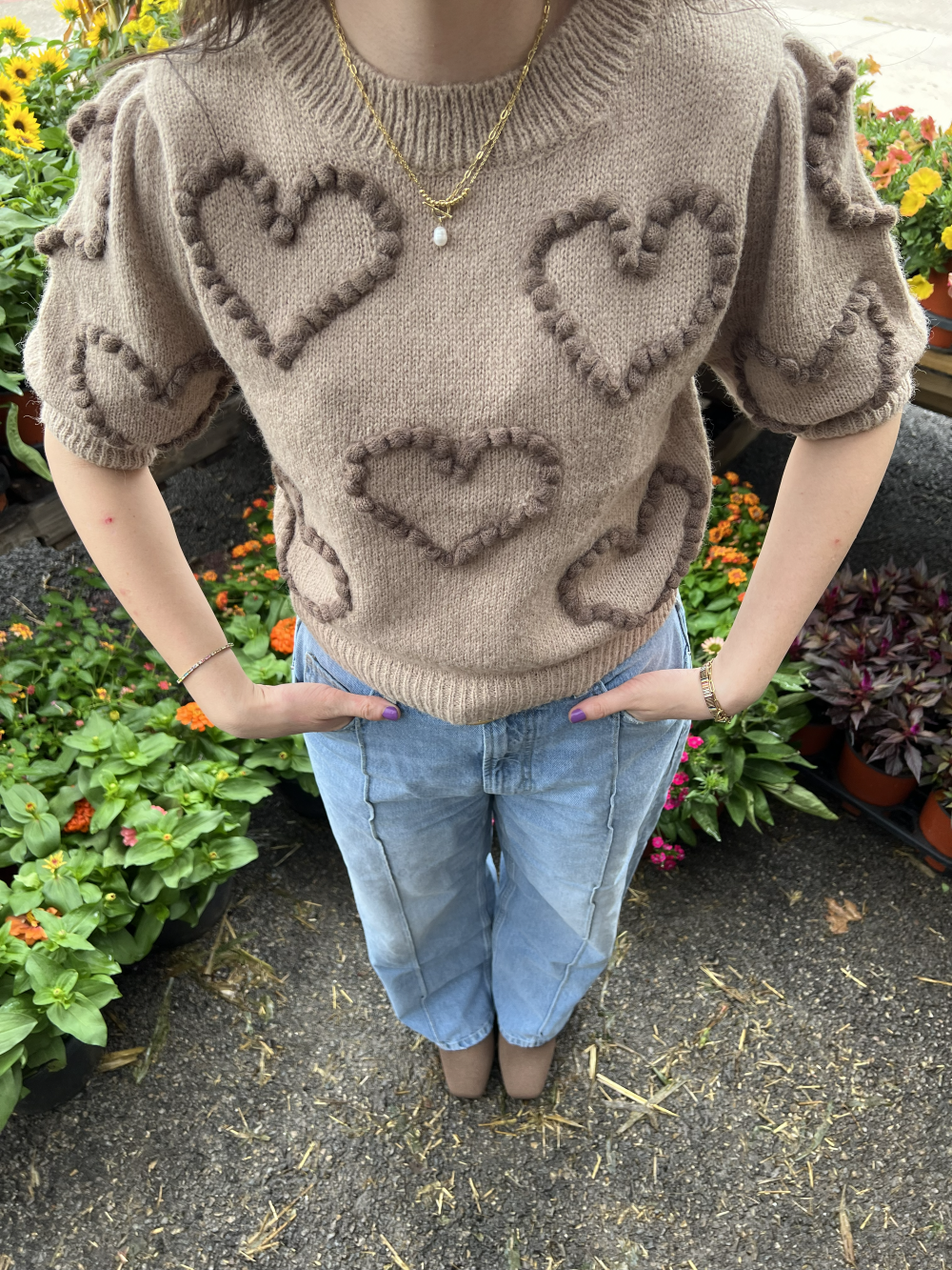 Person wearing a sweater with heart patterns in front of floral plants