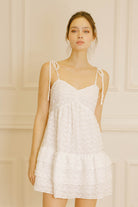 Woman wearing a white textured dress with adjustable thin straps against a beige wall.