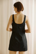 Back view of a woman wearing a black dress with a plain background