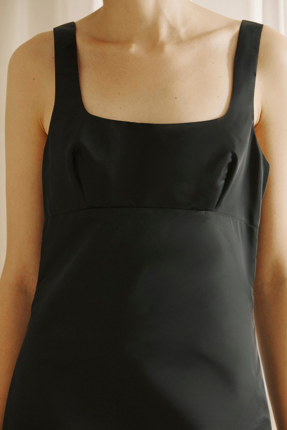 Black sleeveless dress worn by a person against a neutral background
