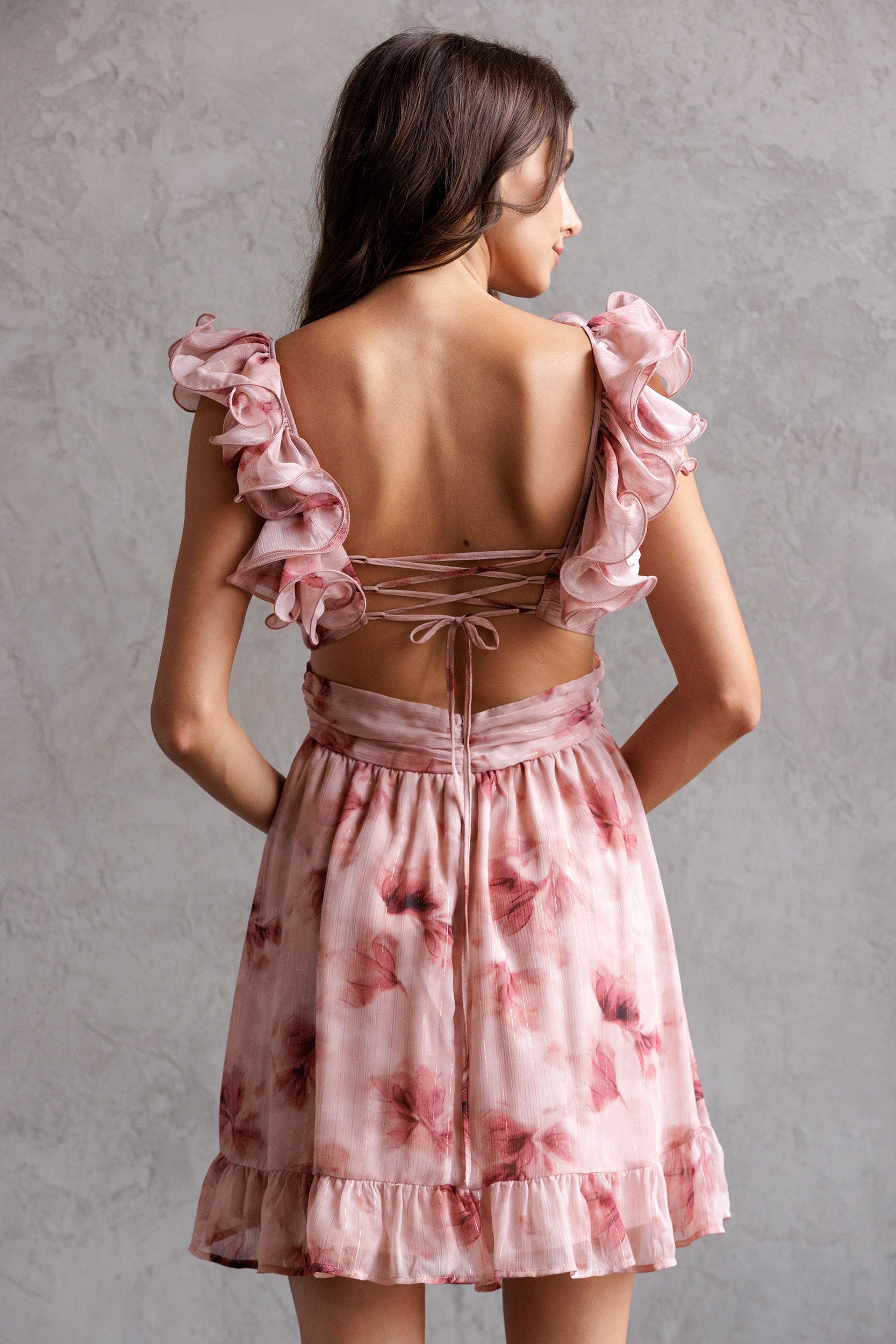 Woman wearing a pink floral dress with ruffled straps against a gray background