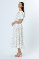 Side view of a woman wearing an ivory with pink rosebuds and flower jacquard print midi dress and beige high-heels on a white background
