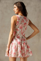Back view of a woman wearing an ivory and pink floral dress against a plain background