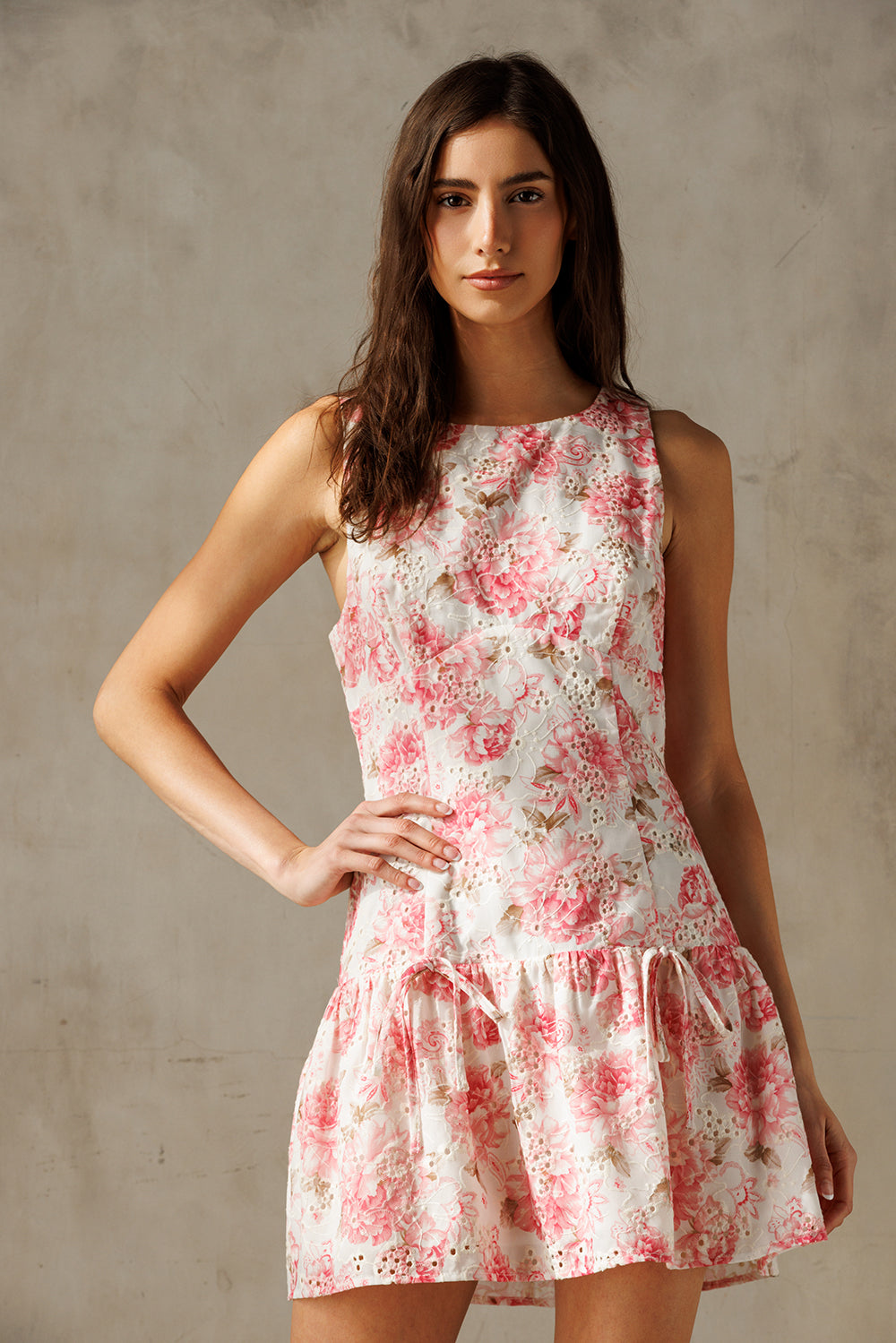A woman wearing an ivory and pink sleeveless, floral print, drop-waist mini dress with a round neckline.