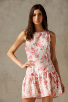 A woman wearing an ivory and pink sleeveless, floral print, drop-waist mini dress with a round neckline.
