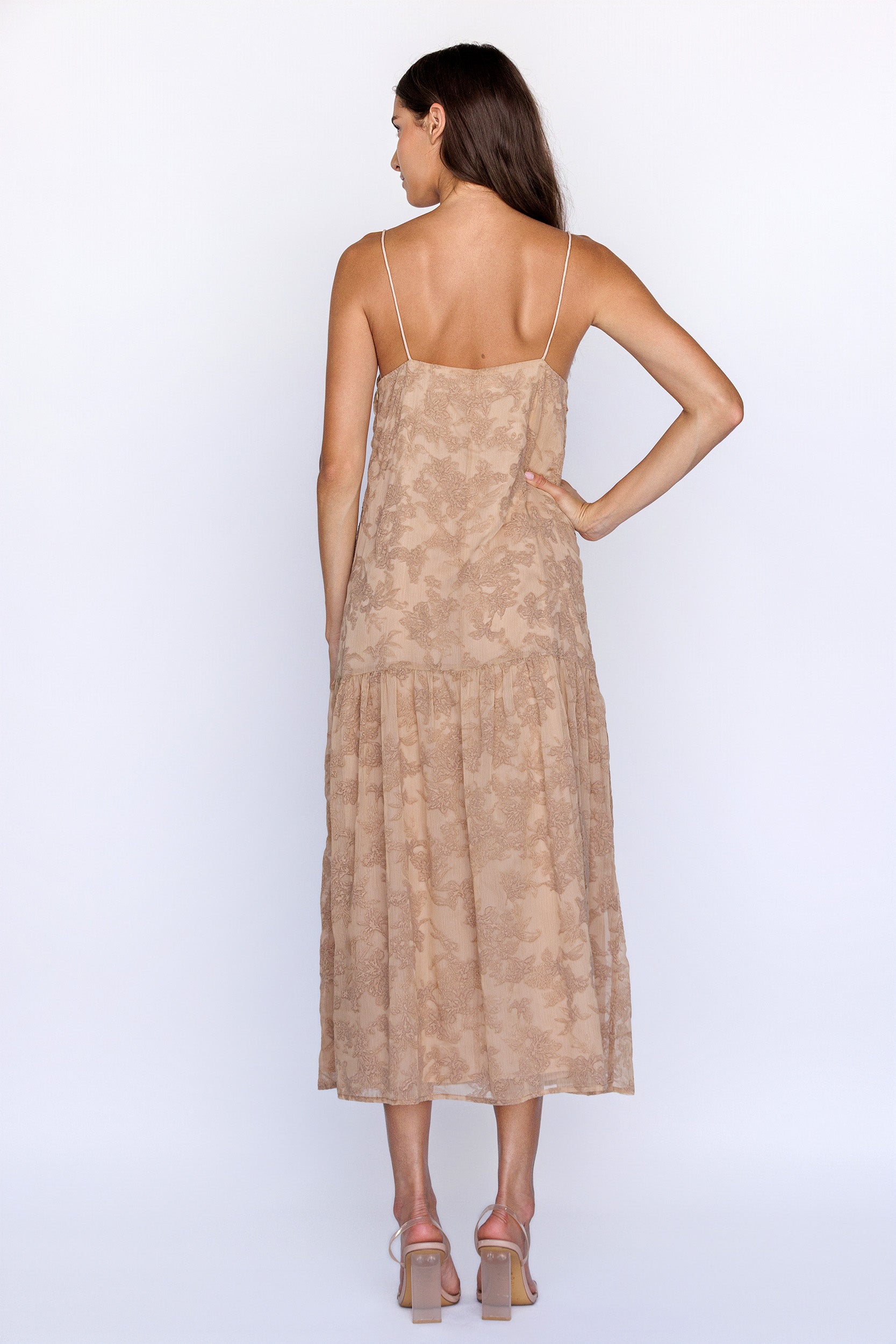Back view of a woman wearing a beige floral textured dress on a white background
