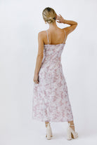 Back view of a woman wearing a lilac floral dress with a slit and beige heels on a white background