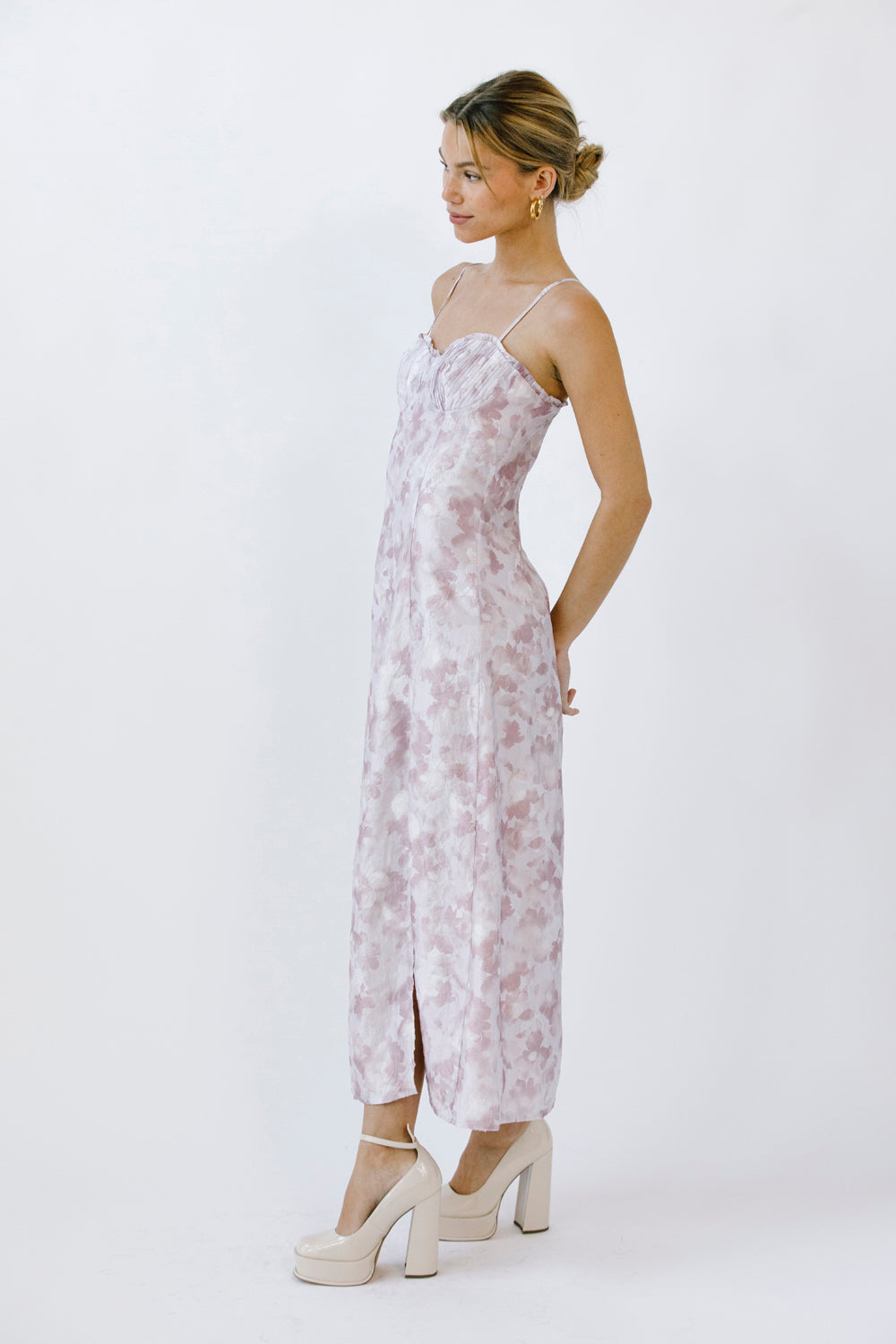 Side view of a woman wearing a lilac floral dress with a slit and beige heels on a white background