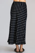 Back view of a black skirt with white polka dots worn by a person on a gray background