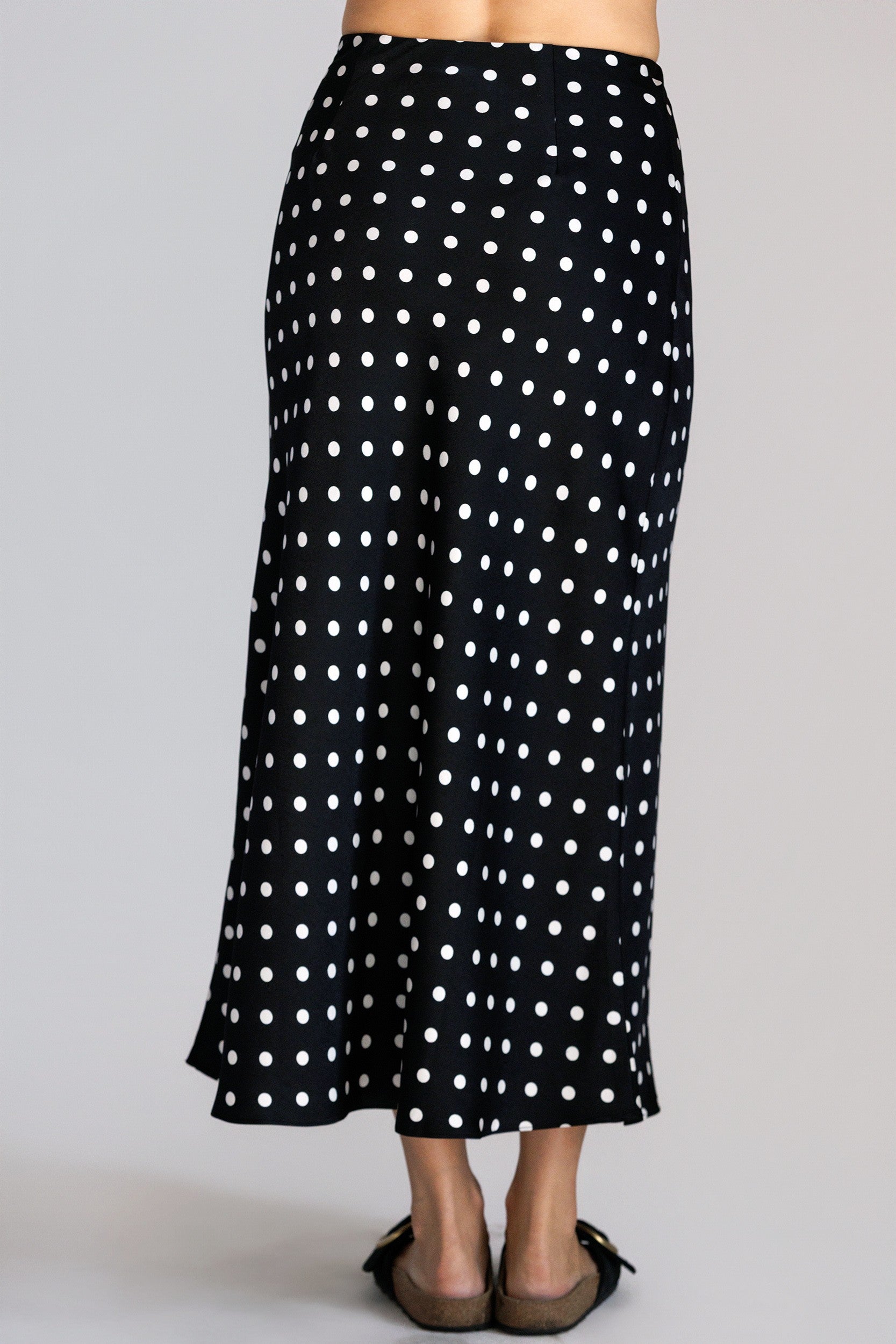 Back view of a black skirt with white polka dots worn by a person on a gray background