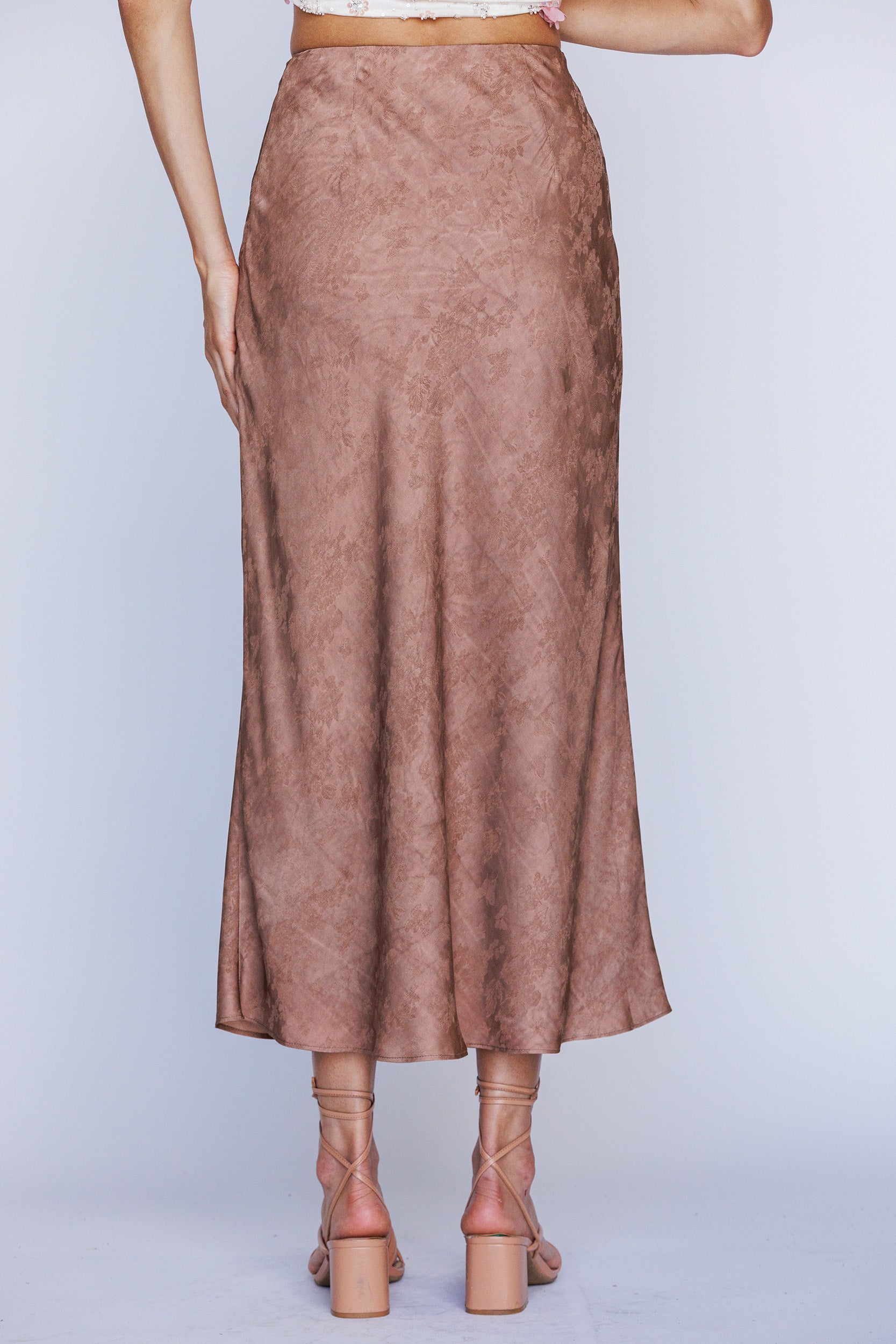 Back view of a brown suede skirt worn by a person on a light gray background