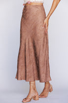 Side view of a brown satin-like skirt worn by a person on a light gray background