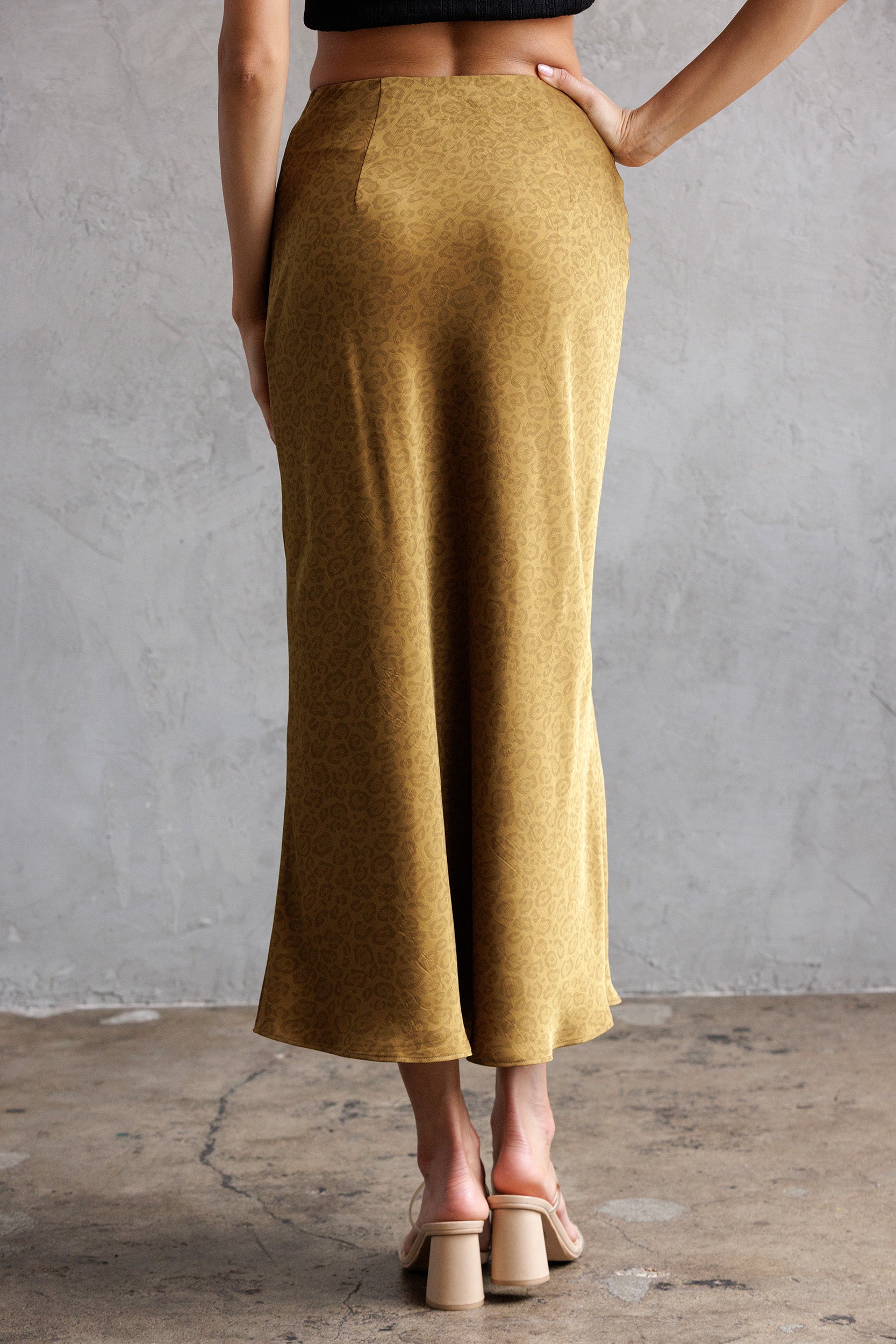 Person wearing mustard yellow midi skirt against a gray wall.