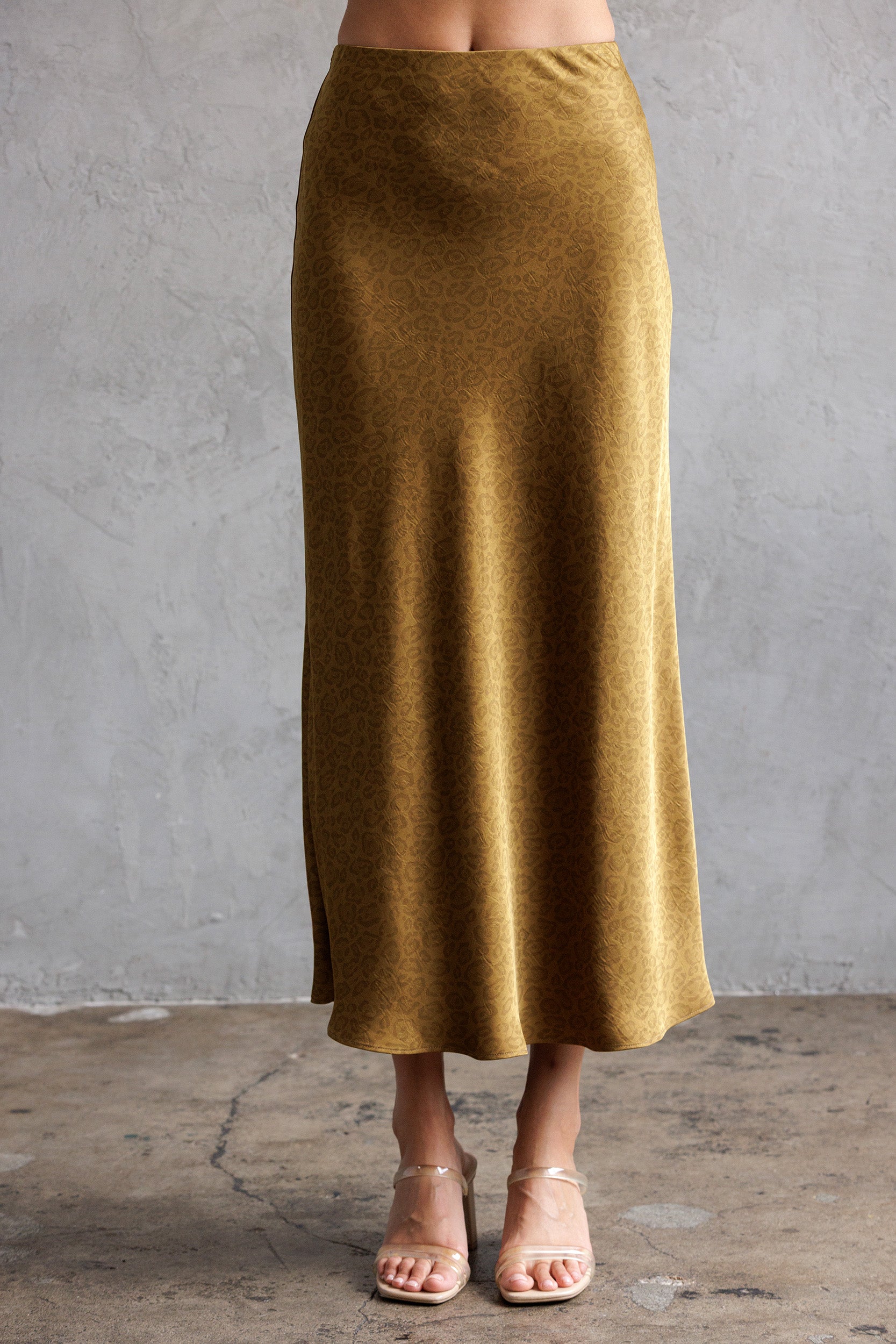 Mustard midi skirt worn by a person against a gray concrete wall.