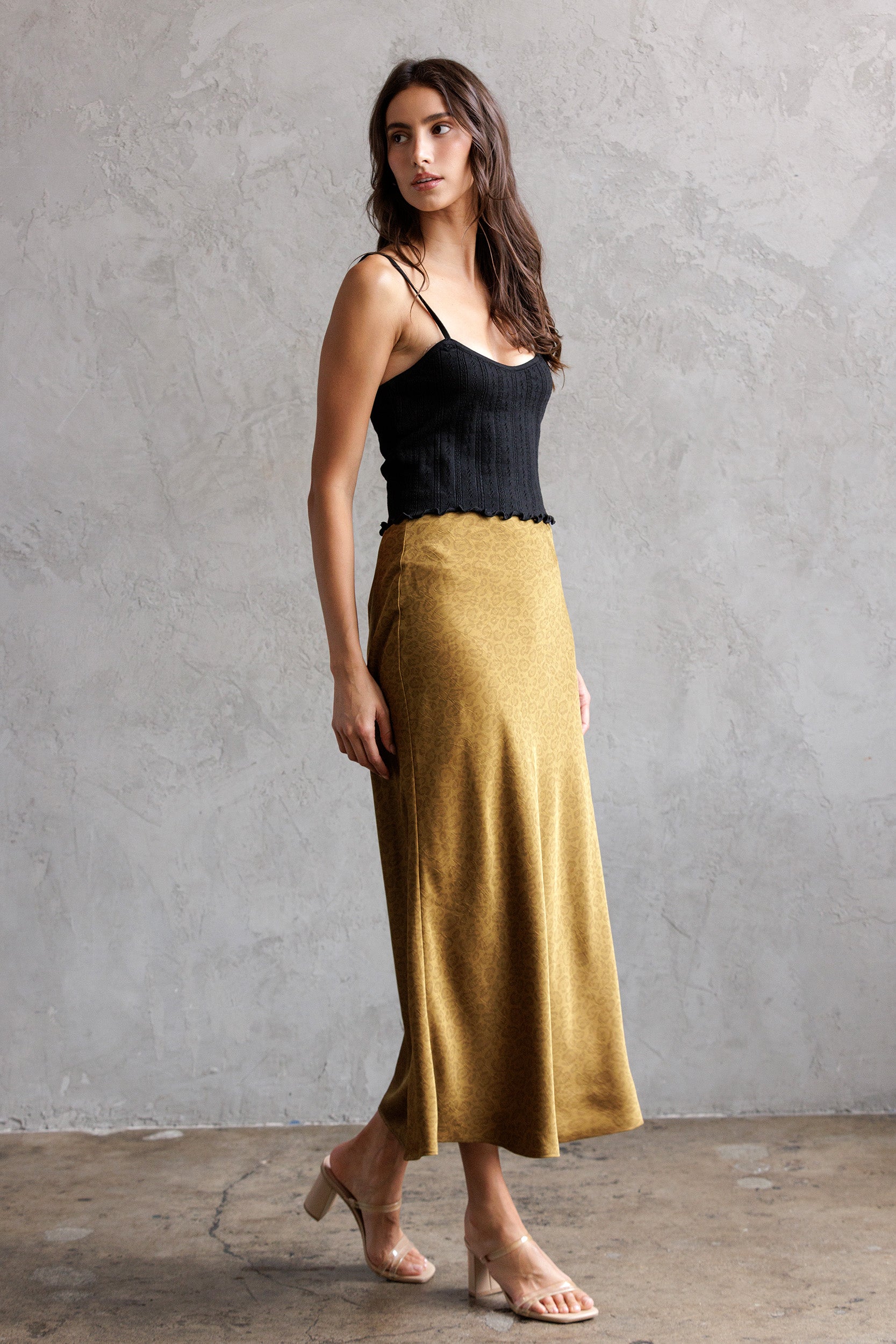 Woman wearing a black top and mustard yellow skirt against a gray wall.