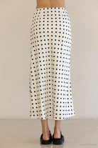 Person wearing a black and ivory polka dot skirt against a plain background