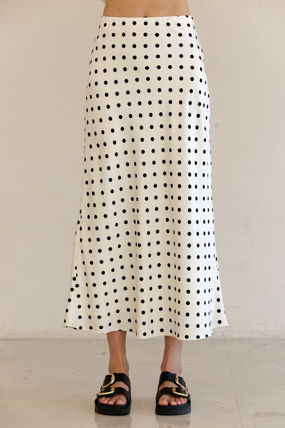 Person wearing an ivory polka dot skirt with a plain background