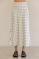Person wearing an ivory polka dot skirt with a plain background