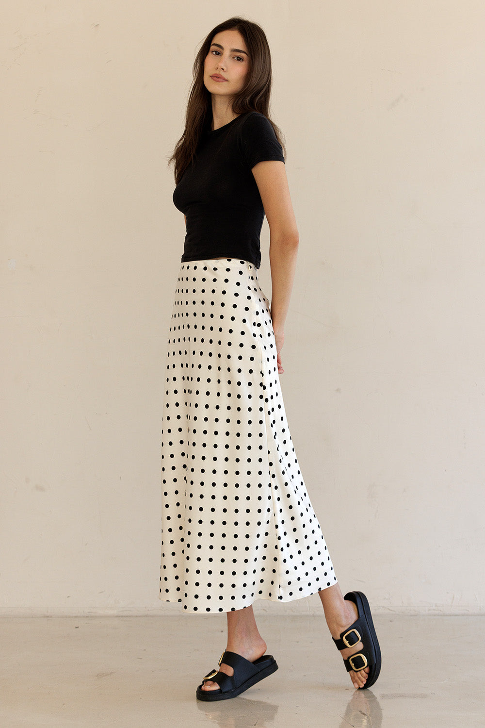 Woman wearing a black top and white polka dot skirt against a beige background