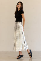Woman wearing a black top and white polka dot skirt against a beige background