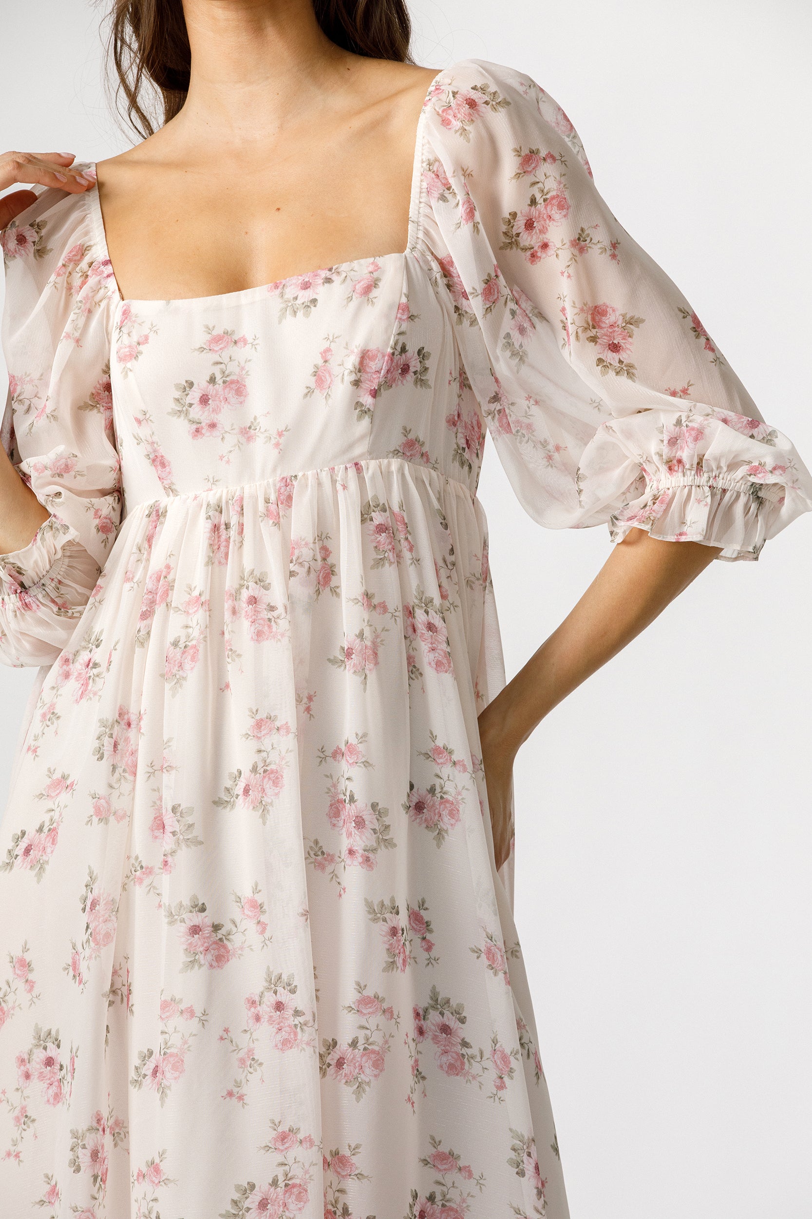 A woman wearing a pink midi dress with a pink and green floral print, featuring puff sleeves and a square neckline, shown against a plain white background.