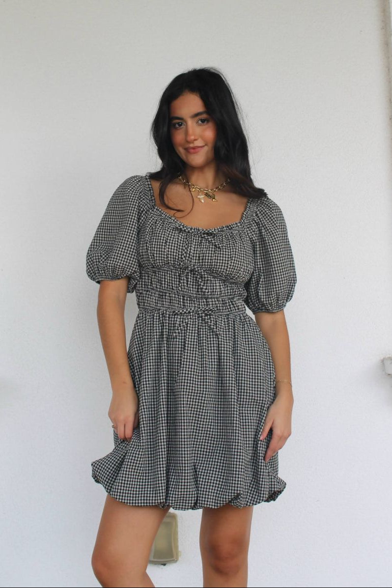 Model wearing a checkered dress standing against a white wall.