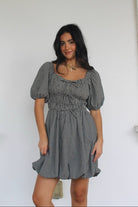 Model wearing a checkered dress standing against a white wall.