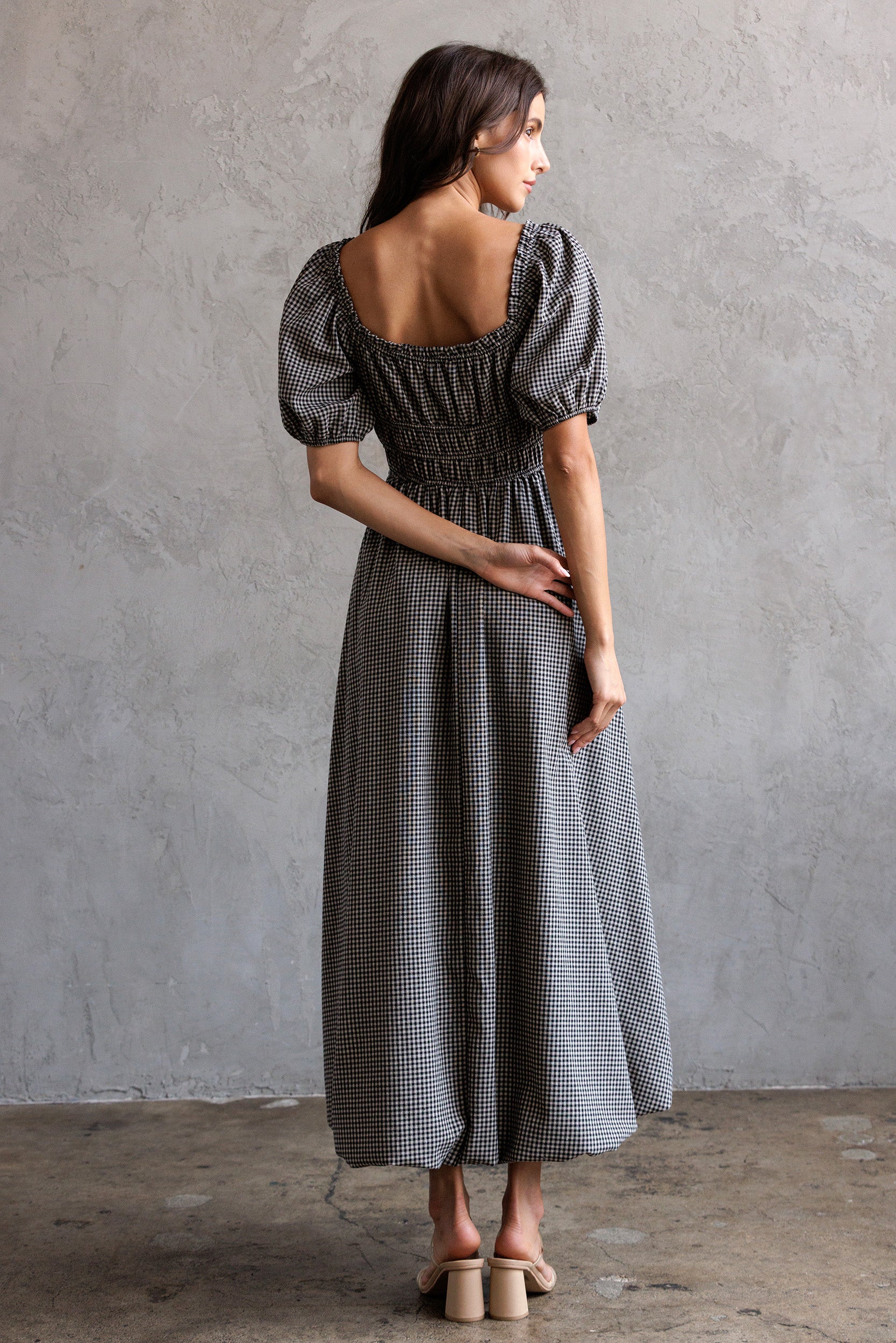 Woman wearing a checkered dress with puff sleeves against a gray concrete wall.