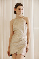 Woman wearing a gold mini dress against a beige curtain background