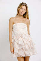 Woman wearing a strapless, ruffled dress against a plain background