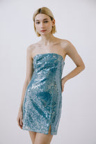 Woman wearing a strapless sequin dress against a plain background