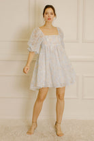 Woman wearing a blue and cream textured dress against a neutral wall.