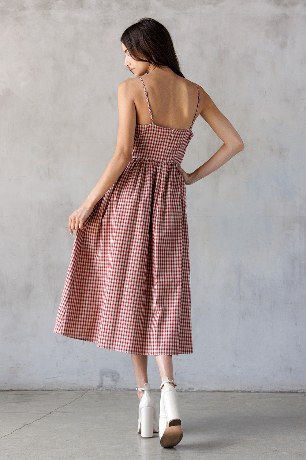 Woman wearing a red and white checkered dress against a gray concrete wall.