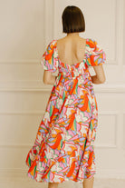 Back view of a woman wearing a colorful patterned dress against a neutral wall.