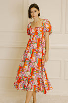 Woman wearing a colorful patterned dress against a neutral wall.
