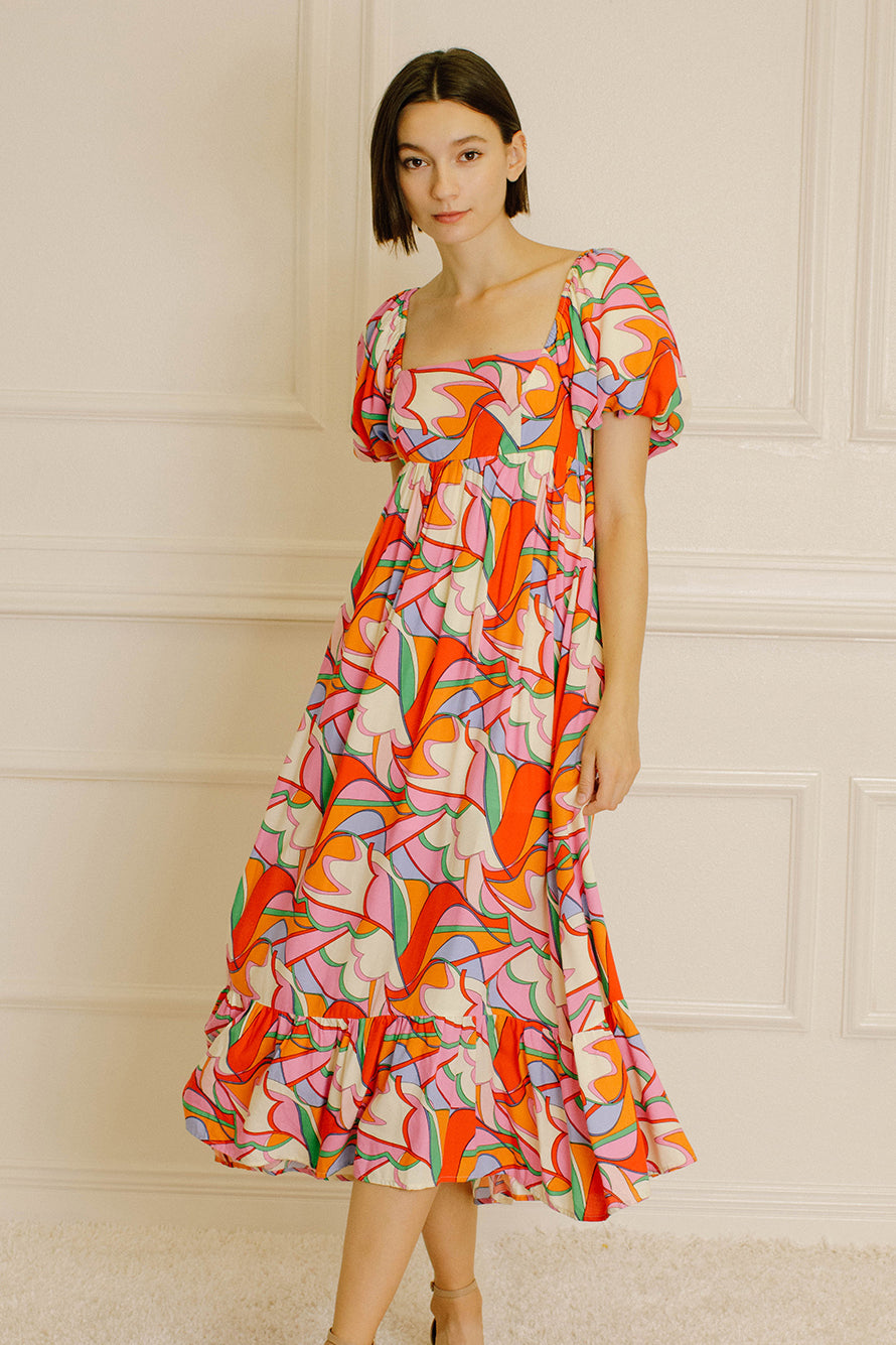 Woman wearing a colorful patterned dress against a neutral wall.