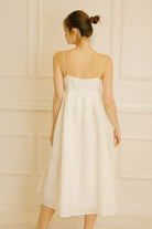Back view of a woman wearing a cream midi dress with floral jacquard details against a light-colored wall