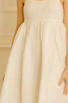A cream dress with floral jacquard details against a light-colored wall