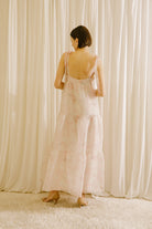 Back view of a woman in a light pink dress standing against a white curtain backdrop