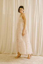 Side view of a woman in a light pink dress standing against a white curtain backdrop