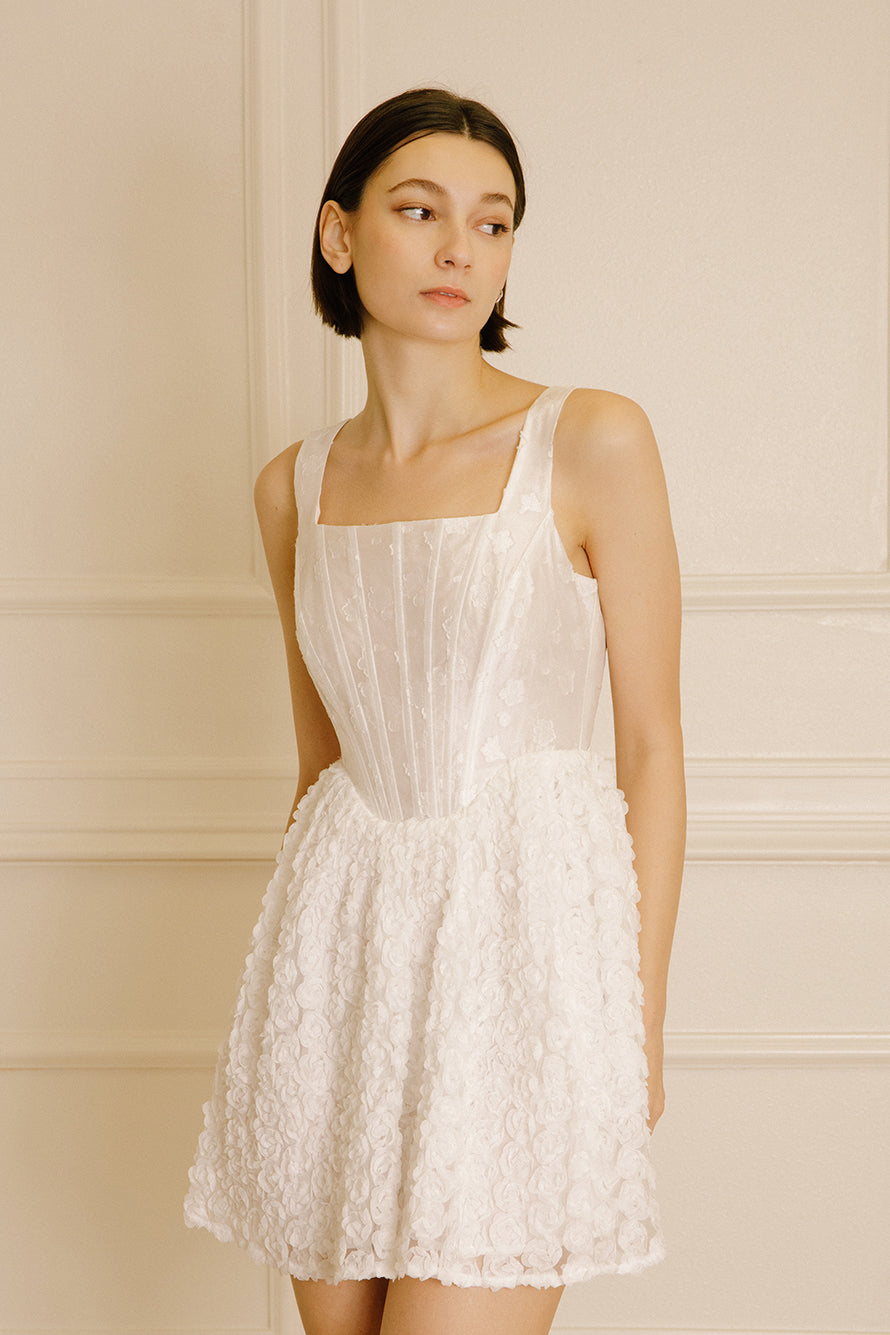 Woman wearing a mini dress with rose appliqués and a structured corset bodice against a neutral wall