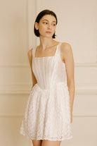 Woman wearing a mini dress with rose appliqués and a structured corset bodice against a neutral wall