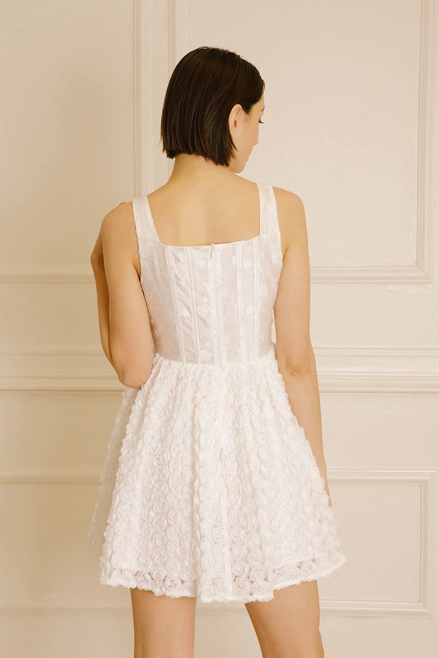 Back view of a woman wearing a mini dress with rose appliqués and a structured corset bodice against a neutral wall