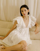 Woman in a white dress with a v-neckline sitting on a beige sofa with a neutral background