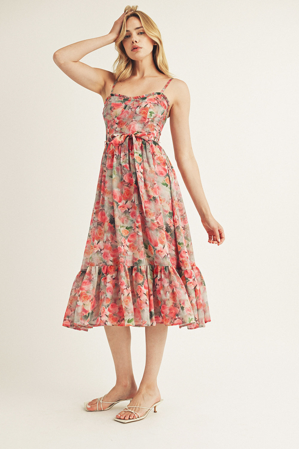 A woman wearing a pink watercolor rose print midi dress with a sweetheart neckline and ruffled hem and white kitten heels